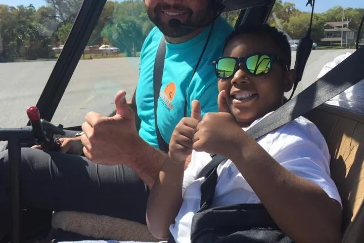 Two people in a helicopter giving thumbs up, both wearing sunglasses.
