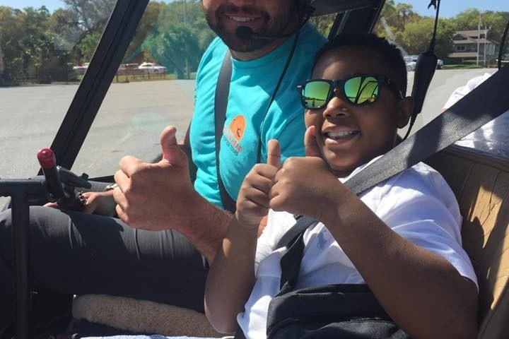 Two people in a helicopter cockpit giving thumbs up, smiling.