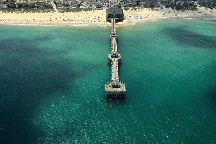 Aerial view of a beach with a pier extending into turquoise water.