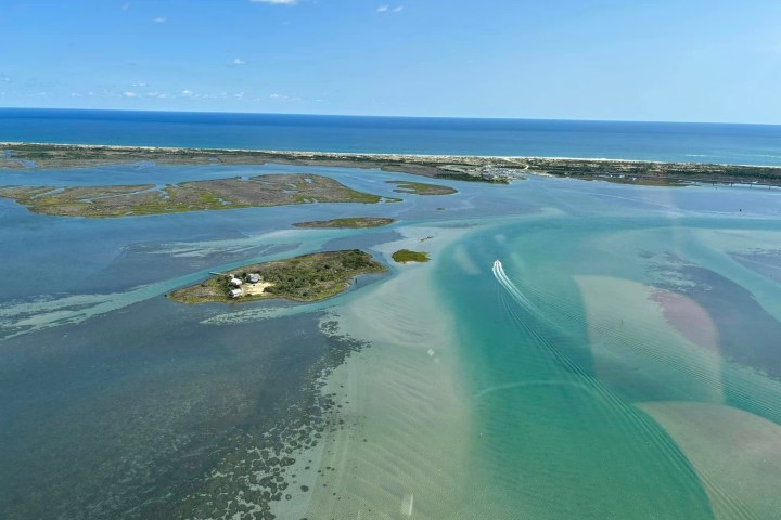 Aerial view of a small island in a blue-green ocean with a boat and distant coastline.